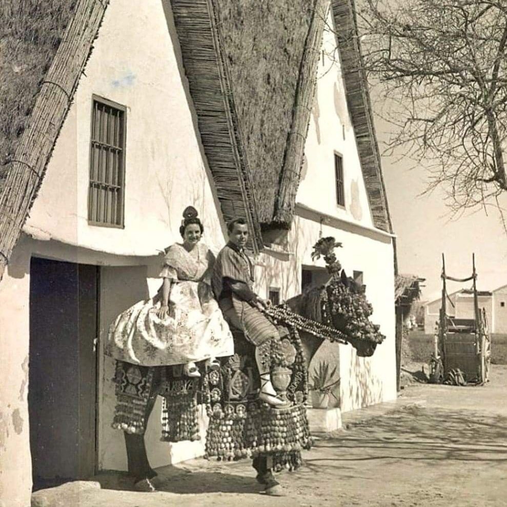 Mujer vestida de valenciana y jinete ante una barraca